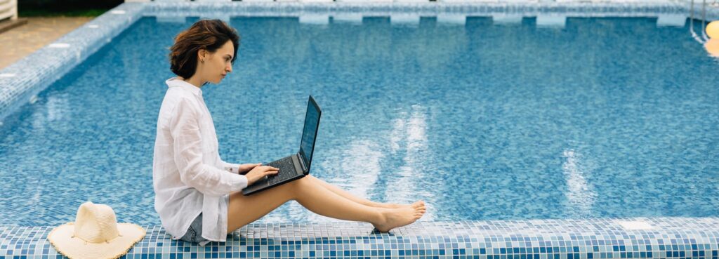 A female travel agent at a pool working on her own travel advisor website | JetSite & Roam