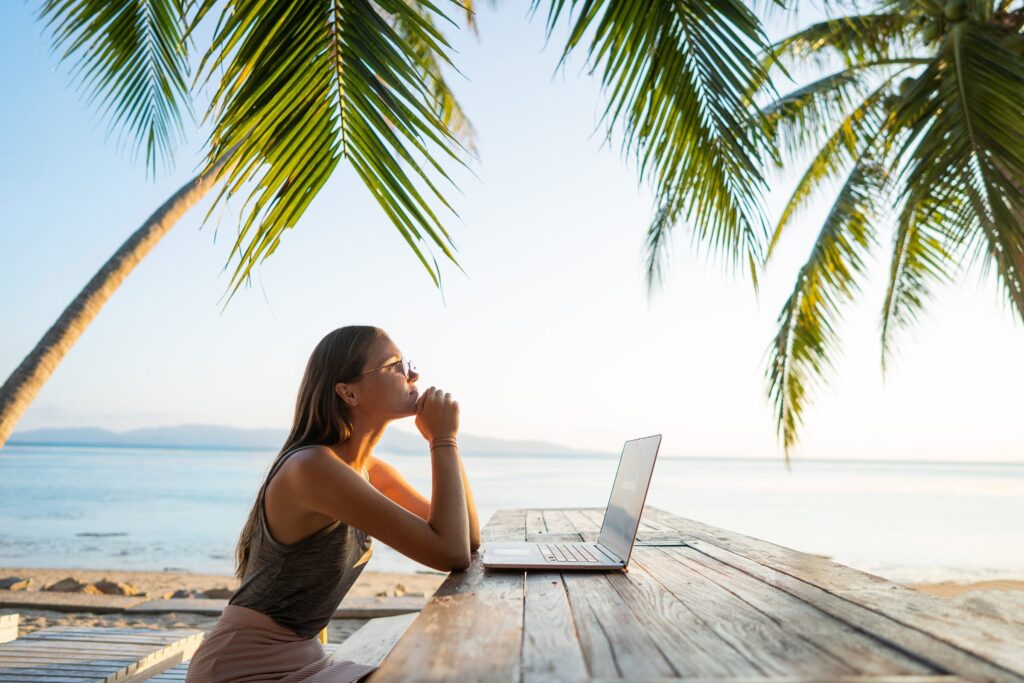 Travel advisor on the beach with a laptop on wooden table, researching the best website builder for travel agents