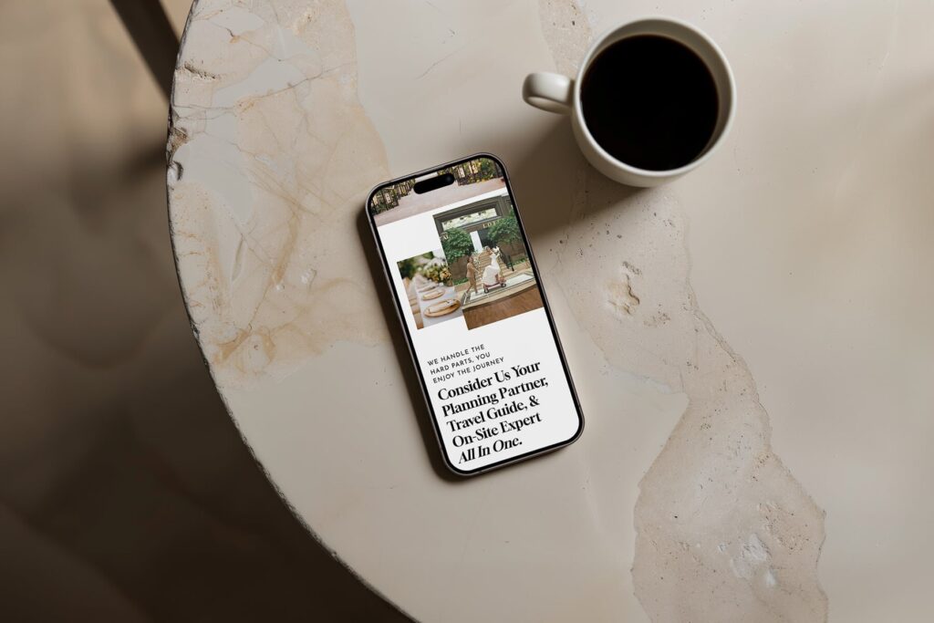 Phone on a stone table with a cup of coffee, a destination wedding planner site on screen, by JetSite & Roam